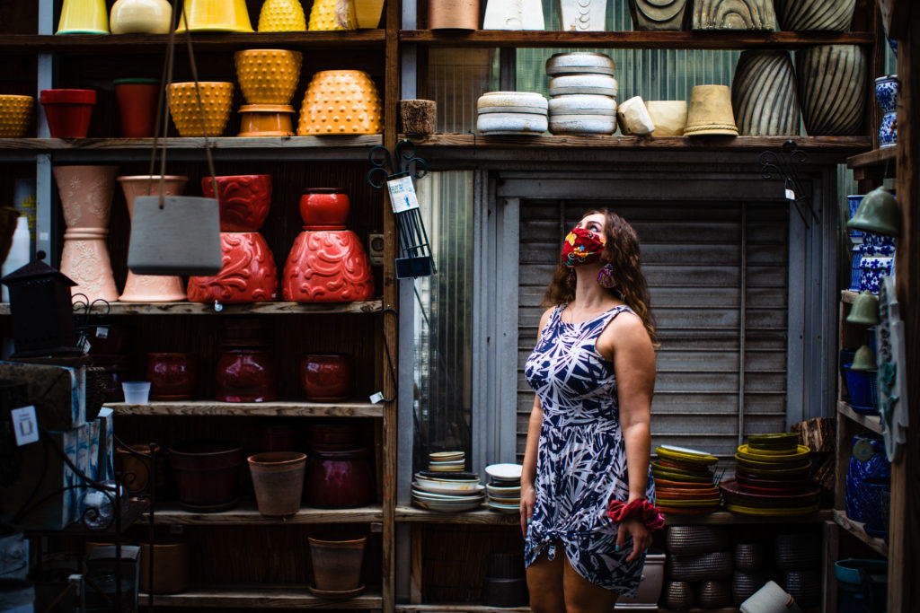 A female in a blue dress, looking up, healing from the sunlight with colorful pots around her.