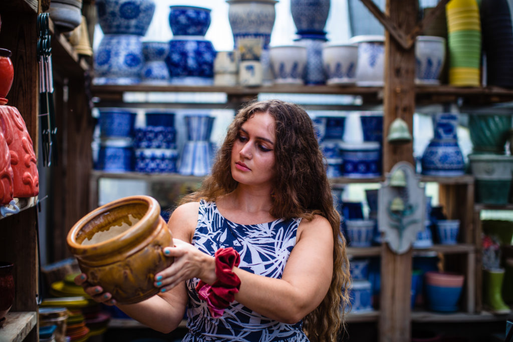 A female in a blue dress thoughtfully looking at a yellow pot. 