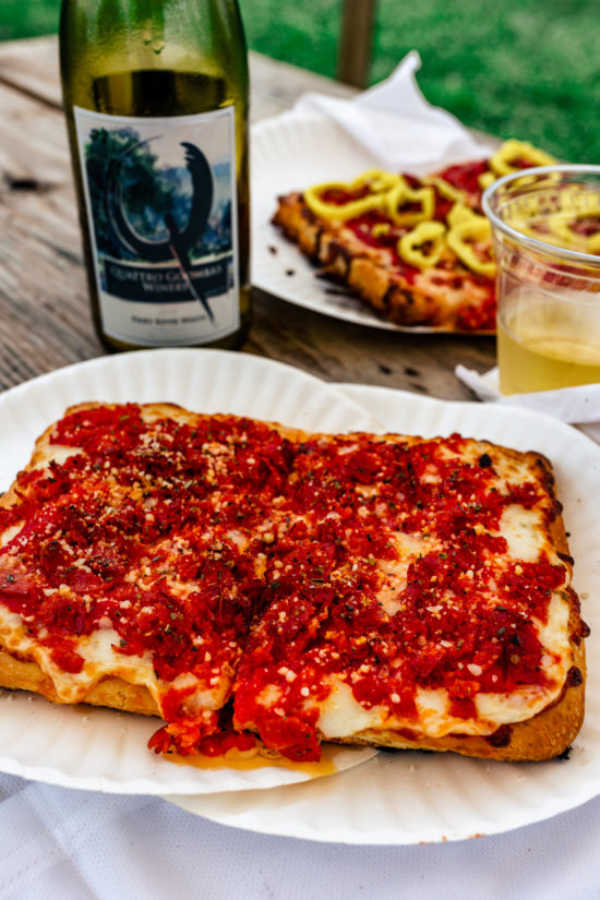 two huge slices of pepperoni pizza in front of a bottle of white wine. There are two more slices of pizza behind the wine with banana peppers on top. 